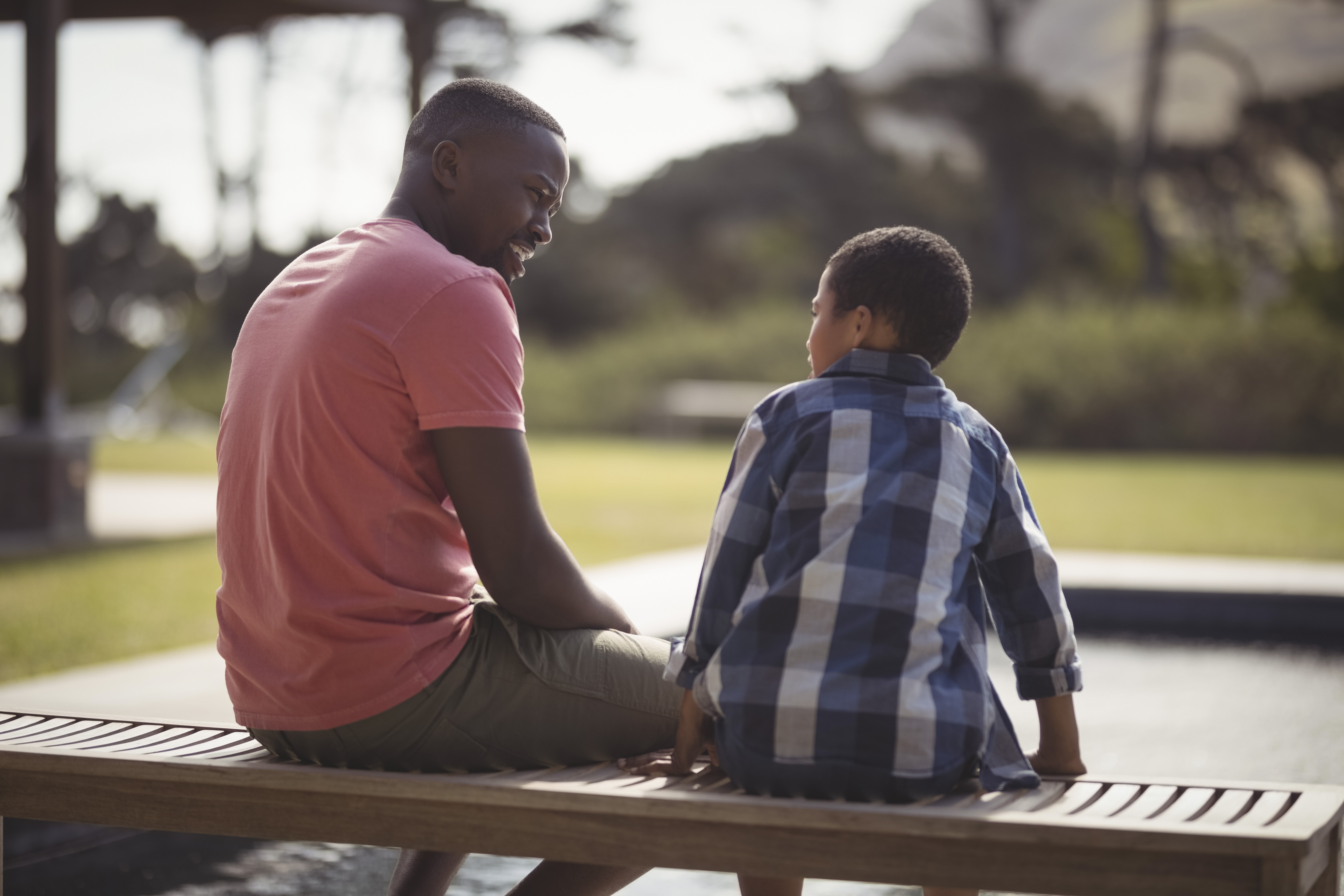 dad sitting on bench with school aged son talking communication listening parent child relationship